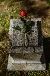 Lonely red rose atop a granite tombstone in an outdoor graveyard setting.